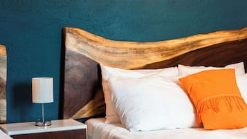 Un lit avec des oreillers blancs et orange, une tête de lit en bois, une table de chevet avec une lampe et une commode de chevet avec un tiroir.