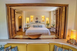 A hotel room with a bed, bedside tables, decorative wall sconces, and a view through an open doorway.