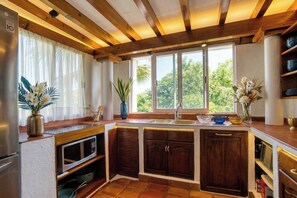 A kitchen with wooden beams, a built-in microwave, and a window with a view of greenery. - Villa Bougainvillea at Villas del Sol (Zihuatanejo)