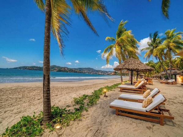 A beach with lounge chairs and a thatched-roof structure.