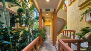 Un couloir avec un escalier, bordé de verdure, menant à une porte portant l’inscription « SORTIE DE ZONE DE PRESSION ».