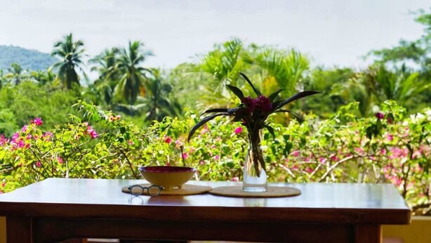 Une table avec un bol et un vase de fleurs, le tout mis en valeur par un décor de verdure luxuriante et un ciel dégagé.