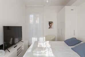 A modern hotel room with a flat-screen TV, a neatly made bed, a chair, and a wardrobe.