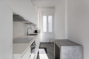 A modern kitchen with white cabinetry, a stainless steel range hood, a black coffee maker, and a clear chair.