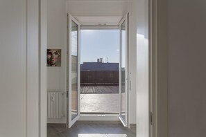 An open door leading to a balcony with a view of buildings and a wooden deck.