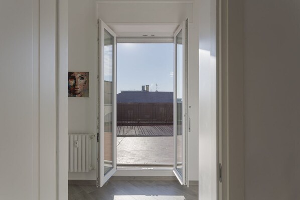 An open door leading to a balcony with a view of buildings and a wooden deck.