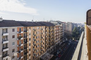 A multi-story residential building with balconies, a street view, and a clear sky.