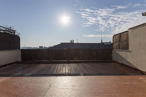 A rooftop terrace with a view of the city skyline, a wooden floor, and a metal fence.