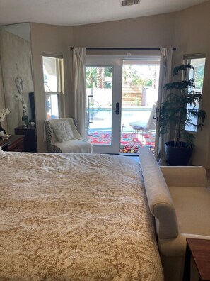 Ein Schlafzimmer mit einem großen Bett, einem Sofa, einer Topfpflanze und Blick auf einen Außenpoolbereich.
