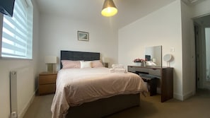 A bedroom with a bed, bedside tables, a dresser, a mirror, and a window with blinds. - Comfy 2 bed house at Wareham train station; the ‘Gateway to the Purbecks’ (Wareham)