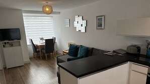 Moderni keittiö, jossa on keskeinen saareke, ruokailutila pöytineen ja tuoleineen sekä oleskelutila, jossa on sohva.