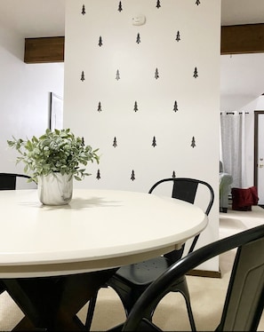 A round dining table with a potted plant, black chairs, and a wall with a pattern of small trees.