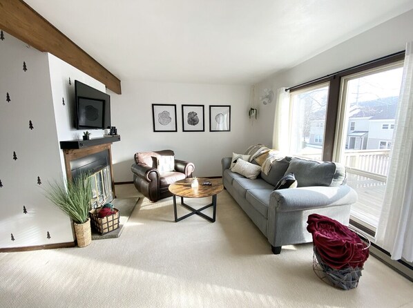 A living room with a fireplace, a sofa, a coffee table, and a TV mounted on the wall.