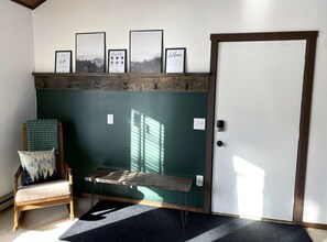 A room with a green wall, a wooden bench, a chair with a cushion, and a door.