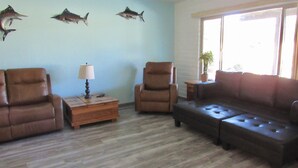 A living room with a brown leather sofa, two armchairs, a wooden side table with a lamp, and a potted plant by a window. - 🌵 Tucson Desert Oasis – 6BR-5BA Home near Golf Courses, University & Shopping (Tucson)