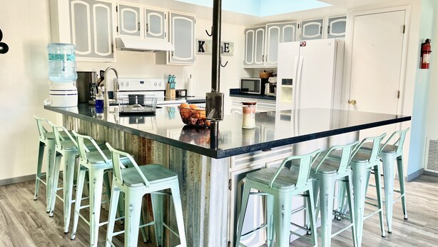 A modern kitchen with a central island, bar stools, and white cabinetry. - 🌵 Tucson Desert Oasis – 6BR-5BA Home near Golf Courses, University & Shopping (Tucson)