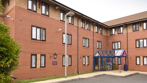 A multi-story brick building with a blue entrance canopy, security cameras, and a sign indicating a parking area. - Premier Inn Birmingham Cc Broad Street (Birmingham)