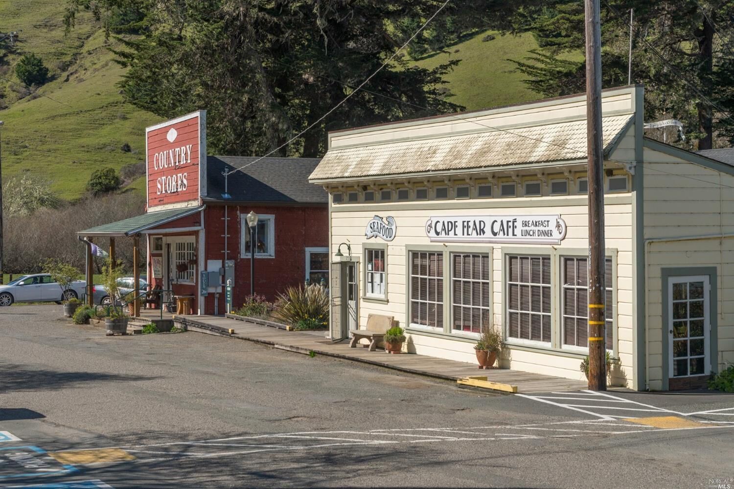 Een straatje in een klein dorp met een bord van Country Stores, een Cape Fear Cafe dat ontbijt en lunch serveert, en een geparkeerde auto.
