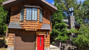 Une maison en bois avec une porte rouge, un garage et une cheminée en pierre.