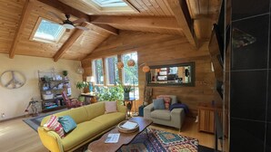 A cozy cabin interior with a high ceiling, wooden beams, a yellow sofa, a patterned rug, and a large mirror reflecting the room.