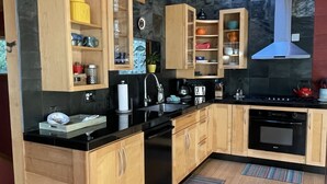 A modern kitchen with wooden cabinets, a black countertop, a built-in oven, and a stone backsplash.