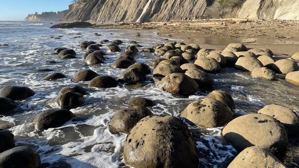 A rocky beach with large boulders and cliffs in the background.