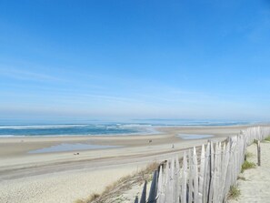 Une plage avec une clôture en bois, un rivage sablonneux et une mer calme sous un ciel dégagé.