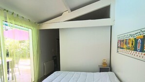 A bedroom with a bed, a window with sheer curtains, a radiator, and a small table with a decorative item. - pleasant villa of 120 qm for 8 people (BISCARROSSE)