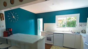 A kitchen with teal walls, white cabinetry, a central island with stools, a large window, and a clock on the wall. - pleasant villa of 120 qm for 8 people (BISCARROSSE)