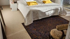 A bedroom with a patterned headboard, a bed with white bedding and yellow pillows, a nightstand with a lamp, and a view through a window. - pleasant villa of around 130m² for 7 people (BISCARROSSE)