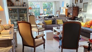 A spacious living room with a sofa, armchairs, and a dining area. There is a view of the outdoors through large windows. - pleasant villa of around 130m² for 7 people (BISCARROSSE)