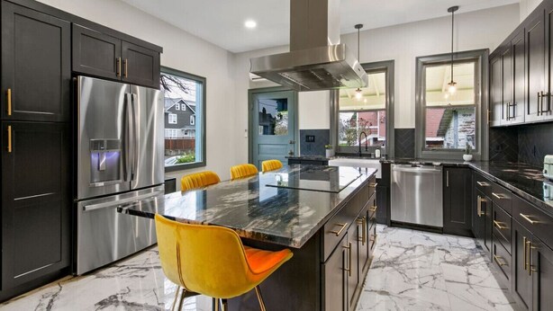 A modern kitchen with dark cabinets, stainless steel appliances, a marble countertop, and yellow chairs. - Casa Van Gogh: a Historic N. Slope retreat (Tacoma)