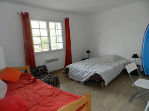 A bedroom with two beds, a window with curtains, a chair, and a desk with a lamp.