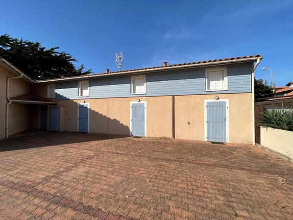 Een gebouw met twee verdiepingen, een pannendak en een kleine antenne op het dak, met een geplaveid binnenterrein met een bakstenen vloer.