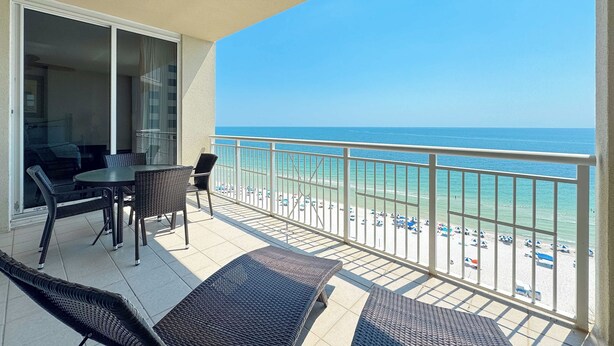 Ein Balkon mit Blick auf den Strand, einem Tisch und Stühlen sowie einer Glasschiebetür, die zu einem Innenraum führt.