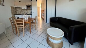 A compact living space with a dining area, a black sofa, and a kitchen in the background.
