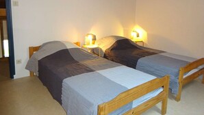 Una stanza con due letti di legno, ognuno dotato di testiera, e un tavolino posizionato tra i due letti. Sopra i letti, sono presenti luci fissate al muro.