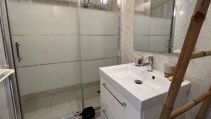 Un bagno moderno con doccia vetrata, un lavandino bianco con uno specchio sopra e una scala di legno appoggiata al muro.