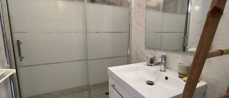 A modern bathroom with a glass-enclosed shower, a white sink with a mirror above it, and a wooden ladder leaning against the wall.