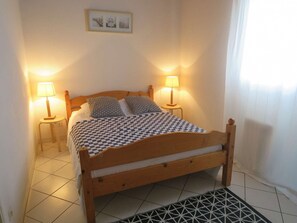 A wooden bed with a checkered bedspread, two bedside lamps, and a framed picture on the wall.
