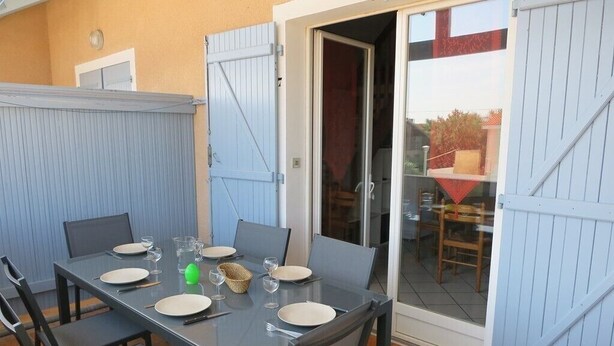 An outdoor dining area with a table set for four, surrounded by chairs, and a sliding glass door leading to an adjacent room. - Apartment on the 1st floor of 45m² for 6 people (BISCARROSSE)