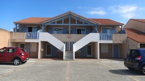 A building with a central staircase, balconies, and a parking area with two cars. - Apartment on the 1st floor of 45m² for 6 people (BISCARROSSE)