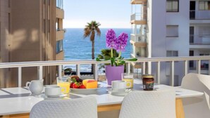 Ein Balkon mit Frühstückstisch, mit Blick auf ein Gewässer und Palmen.