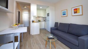 Ein modernes Wohnzimmer mit einem grauen Sofa, einem Glastisch und einem Essbereich mit einem weißen Tisch und Stühlen.