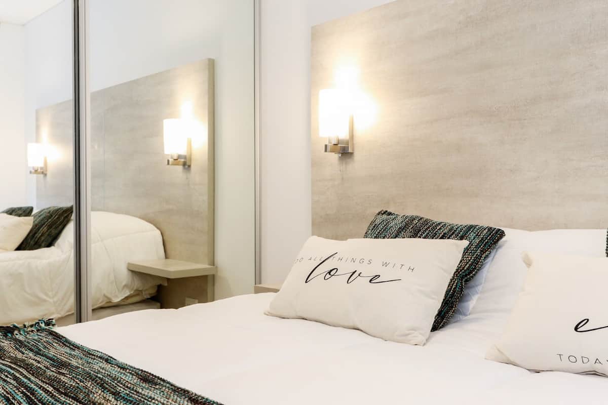 Una habitación de hotel moderna con una cama grande, dos mesitas de noche, un espejo y luces fijadas a la pared.