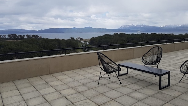 Een terras met uitzicht op een meer en bergen, met een tafel en stoelen.