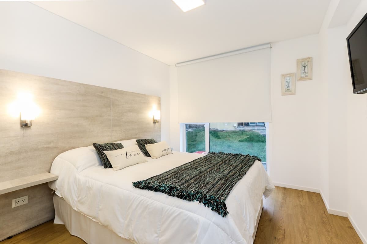 Un dormitorio con cama, mesitas de noche, televisor y ventana con vistas.