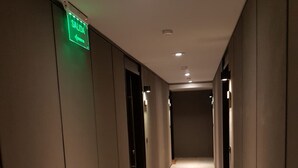 Een gang met een groen EXIT-bord, inbouwspots en een betegelde vloer.