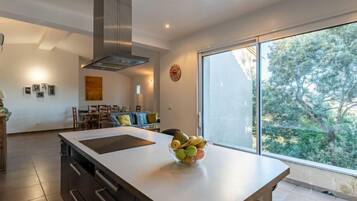 Une cuisine moderne dotée d’un grand îlot central, d’une cuisinière intégrée et d’une grande fenêtre donnant sur la verdure.