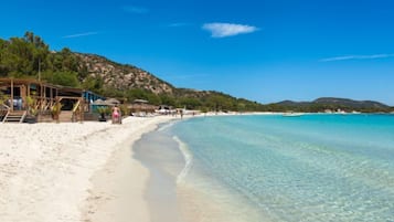 Une plage avec une eau turquoise et limpide, du sable blanc et une structure en bois avec des marches descendant vers la plage.